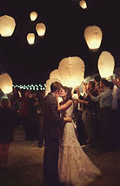 a bride and groom kissing in front of floating paper lanterns at the end of their wedding day