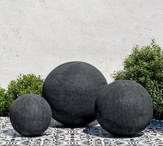 three black balls sitting on top of a white and black tile floor next to bushes