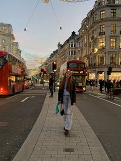 a woman is walking down the street in front of double decker buses