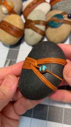 a hand holding a rock with leather wrapped around it and other rocks in the background