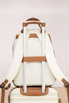 a white backpack with brown straps and two wheels on top of the bag is sitting on a wooden floor