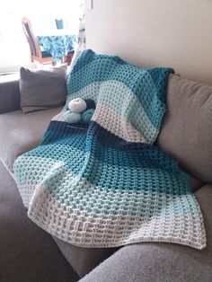 a crocheted blanket sitting on top of a gray couch next to a window