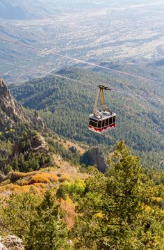 a gondola in the middle of a mountain with trees and mountains behind it