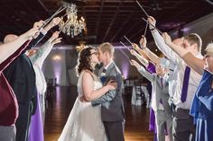 a bride and groom kissing on the dance floor with their arms in the air as they are surrounded by guests