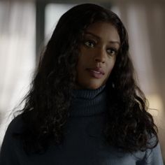 a close up of a person wearing a turtle neck sweater and long curly dark hair