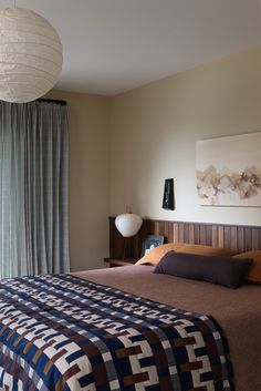 a bed sitting next to a window in a bedroom under a white light hanging from a ceiling fan