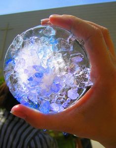 a person holding a glass ball in their hand with ice on it and blue lights inside