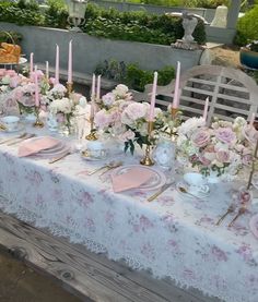 the table is set with pink and white flowers, candles, and plates on it