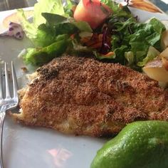 a white plate topped with fish next to a salad and a fork on top of a table