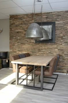 a dining room table and chairs in front of a stone wall with pendant lights hanging from the ceiling