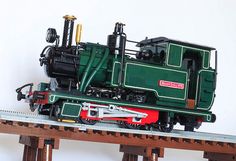 a green and red train engine sitting on top of a wooden track next to a white wall