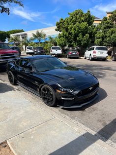 a black car parked on the side of a road next to a parking lot with other cars