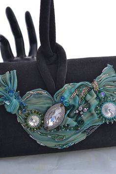 Beautifully beaded and embellished Shibori Ribbon accents this little black evening bag with shades of seafoam green, turquoise blue and forest green. Its covered with Swarovski crystals in various sizes and shapes, and its embellished on both sides! Hand beaded by me in my Las Vegas studio, this striking evening bag measures approximately 7 inches wide, almost 4 1/2 inches tall, and about 2 inches wide, just big enough to tuck in your cell phone, mad money, and a lipstick or two, for that great Luxury Turquoise Evening Bag, Elegant Turquoise Bag For Formal Occasions, Green Beaded Evening Bag, Luxury Green Beaded Bags, Elegant Green Evening Bag, Elegant Green Beaded Evening Bag, Shibori Ribbon, Mad Money, Embroidered Purse