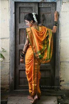 a woman in an orange and green sari is standing by a door with her hand on the back of her head