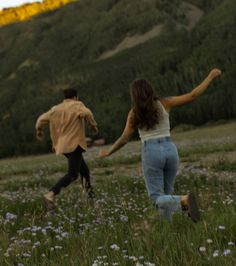 two people running through a field with wildflowers