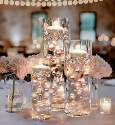 candles and flowers in vases on a white table cloth with lights behind them at a wedding reception