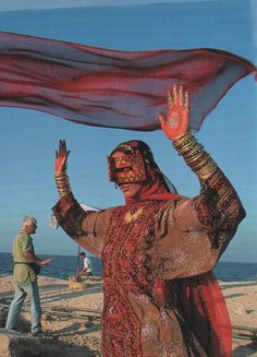 a woman in red and gold is holding up a scarf on the beach with her hands