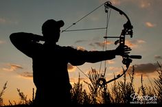 the silhouette of a man with a bow and arrow in his hands, standing next to tall grass