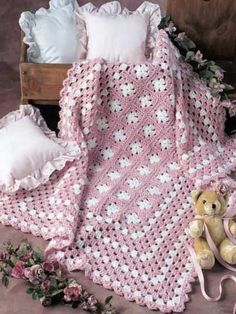 a crocheted blanket, teddy bear and pillow on the floor next to it