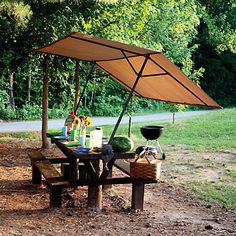 a picnic table set up in the middle of a park with an umbrella over it