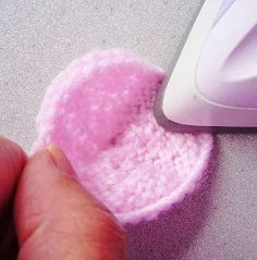 a hand is pressing the button on a pink piece of crochet