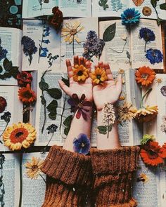 two hands with flowers on top of an open book, surrounded by books and flowers