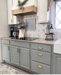 a kitchen with white cabinets and gray counter tops is decorated with greenery on the window sill