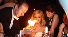 a man and woman are looking at a birthday cake with a lit candle in front of them