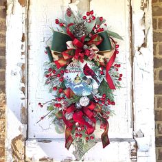 a christmas wreath hanging on the side of a door with red ribbon and pine cones