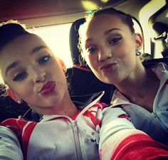 two young women sitting in the back seat of a car, one with her tongue out