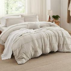 a bed with white comforter and pillows in a room next to a window on the floor