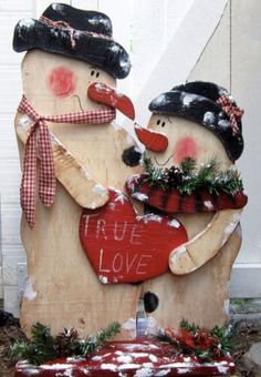 two wooden snowmen holding a red heart