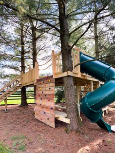 a wooden play structure with a slide and climbing wall in the middle of a wooded area