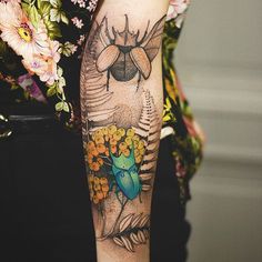 a person with a tattoo on their arm holding a flower and a bug in the background