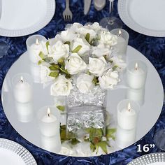 the table is set with white roses and candles for an elegant centerpiece, along with silverware