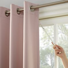 a woman is opening the curtains in front of a window with pink drapes on it