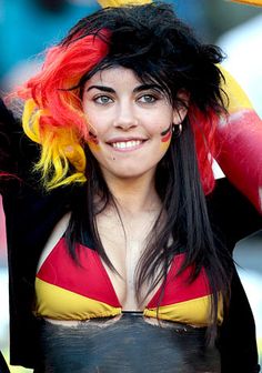 a woman with long black hair wearing a red and yellow wig smiles at the camera