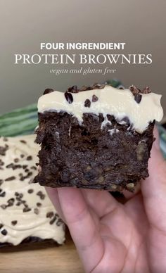 a hand holding a chocolate brownie with white frosting