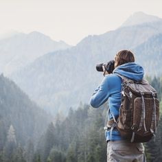 a person with a backpack and camera taking pictures in front of some mountain range covered in trees