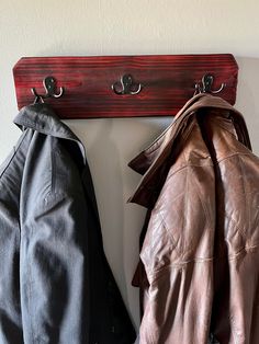 two coats are hanging on a coat rack with leather jackets attached to the hangers