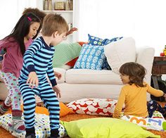 three children playing in the living room with pillows on the floor and toys all around them