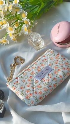 a purse sitting on top of a white sheet next to a pink bottle and flowers