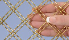 a hand holding a piece of gold colored metal mesh with small holes in the middle