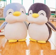 two stuffed penguins sitting next to each other on a wooden floor