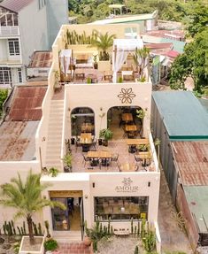 an aerial view of a building with tables and chairs on the roof, surrounded by palm trees