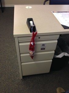 an office cubicle with a red tie hanging from it's drawer