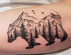 a bear tattoo on the arm with mountains and birds in the sky behind it,