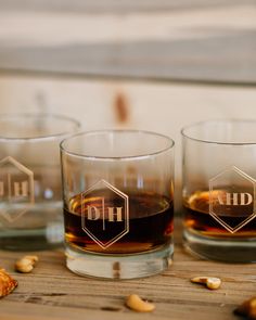 three glasses filled with liquid sitting on top of a wooden table next to nuts and bread