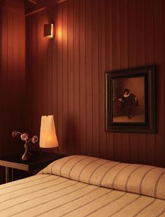 a bedroom with red wood paneling and a painting on the wall above the bed