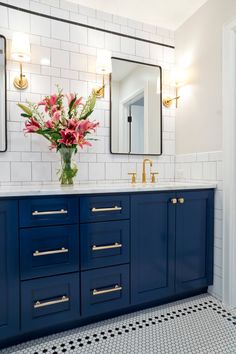 a bathroom with blue cabinets and two mirrors on the wall next to a vase filled with flowers